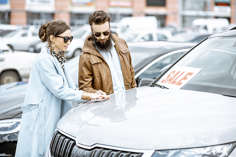 Man and woman choosing used car to buy outdoors