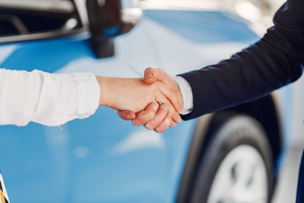 Shaking hands next to a car