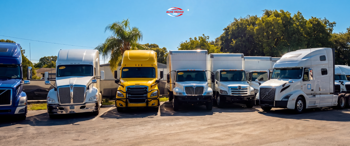 d8b2e0ff-fea1-46ba-b66b-85b656ec4cb3 Commercial semi-trucks and box trucks parked in an outdoor lot.