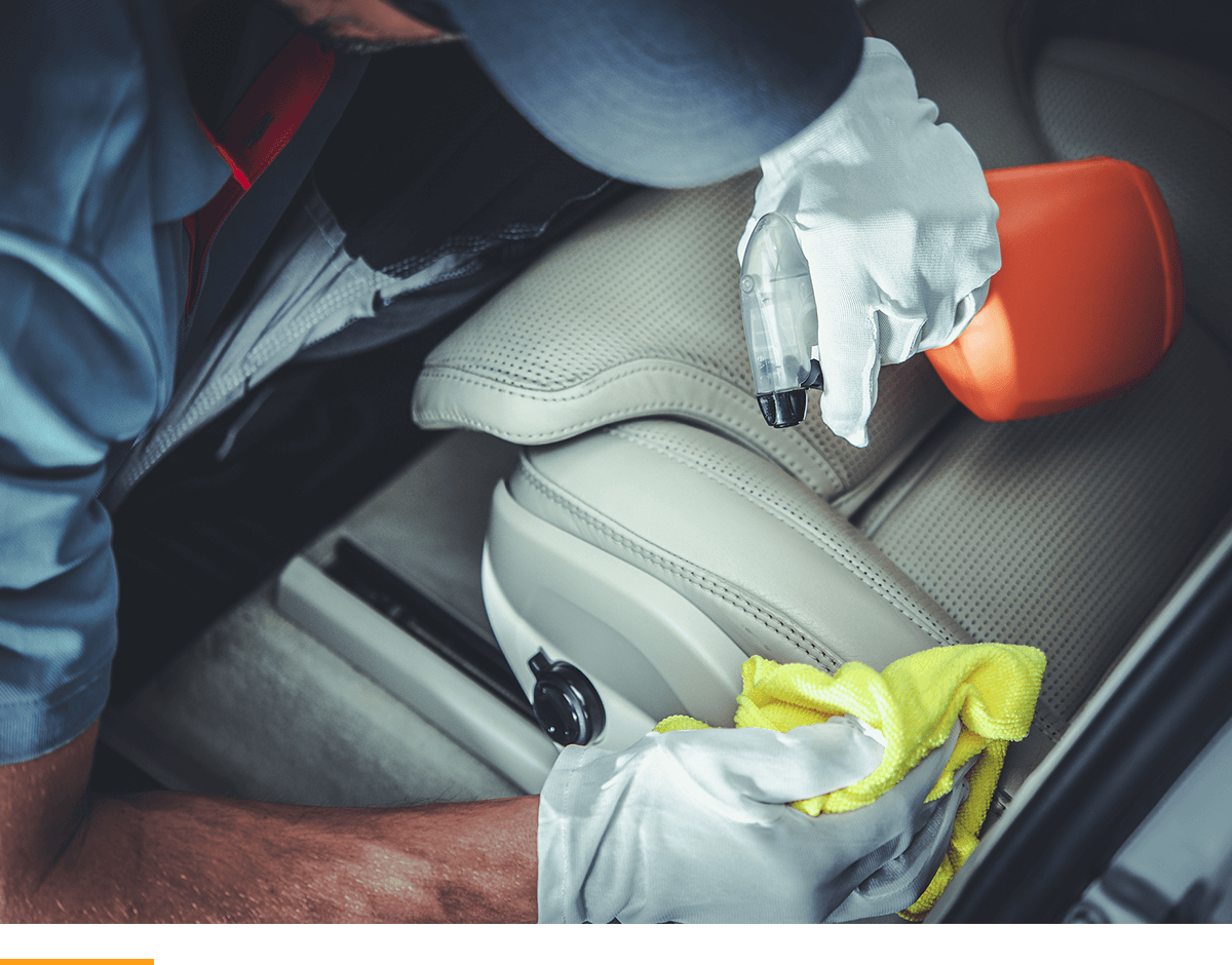 Man spraying cleaning solution on to a car seat and rubbing it off with a cloth. 