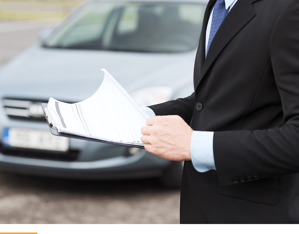 Man standing in a parking lot looking at a clipboard in front of a car. 