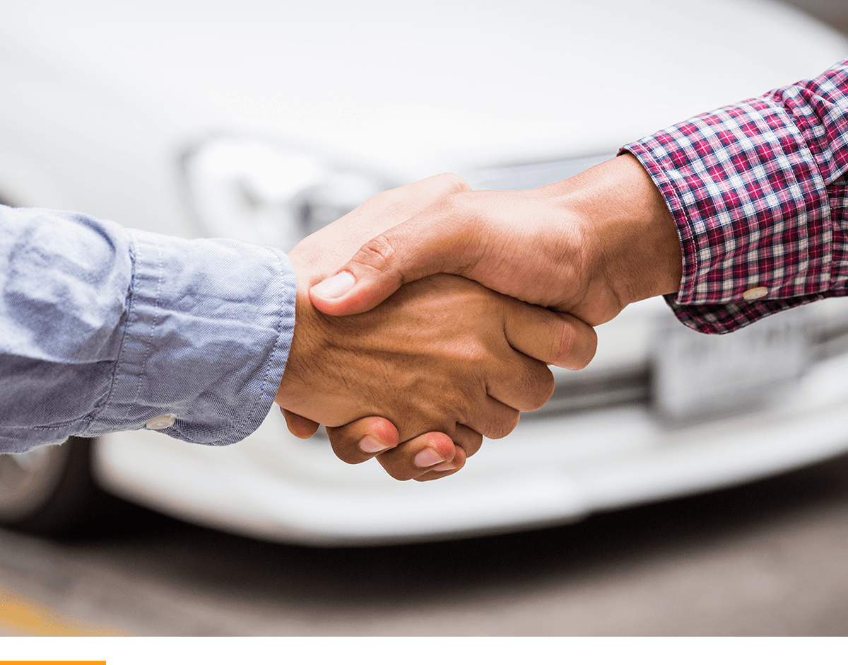 Two people shaking hands in front of a car. 