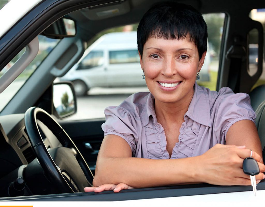 Woman leaning out the window of a car with keys in her hand, smiling. 