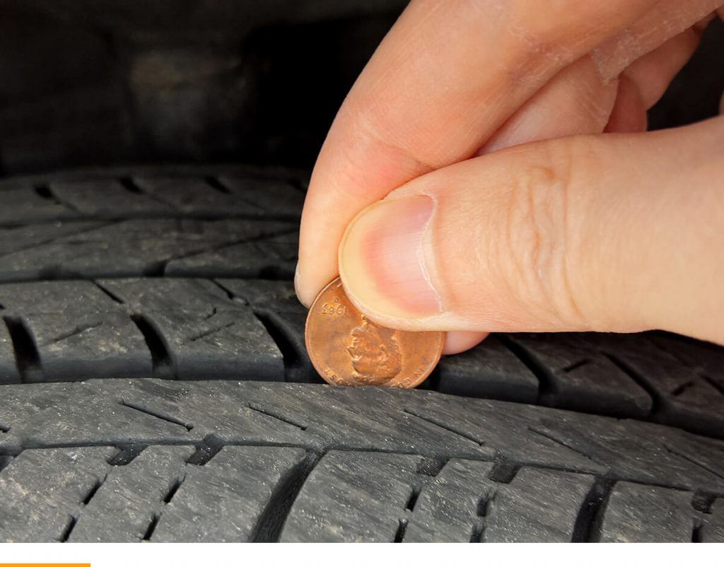 A person holding a penny in a tire to check the tread.