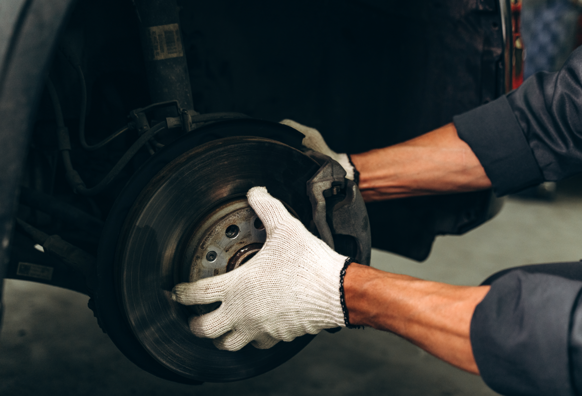 Mechanic wearing gloves inspecting and working on a car’s brake disc system.