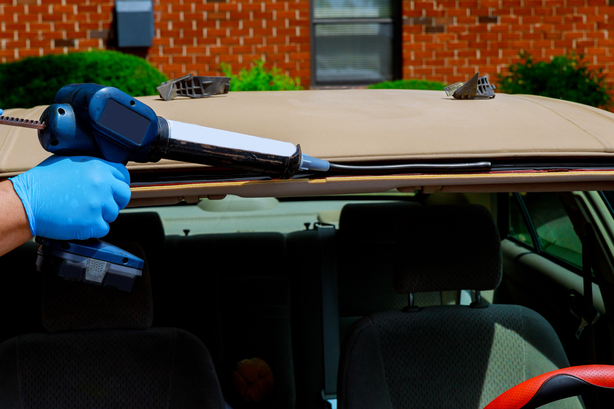 Auto Repair Technician applying sealant to the edges of a car windshield during a replacement process.