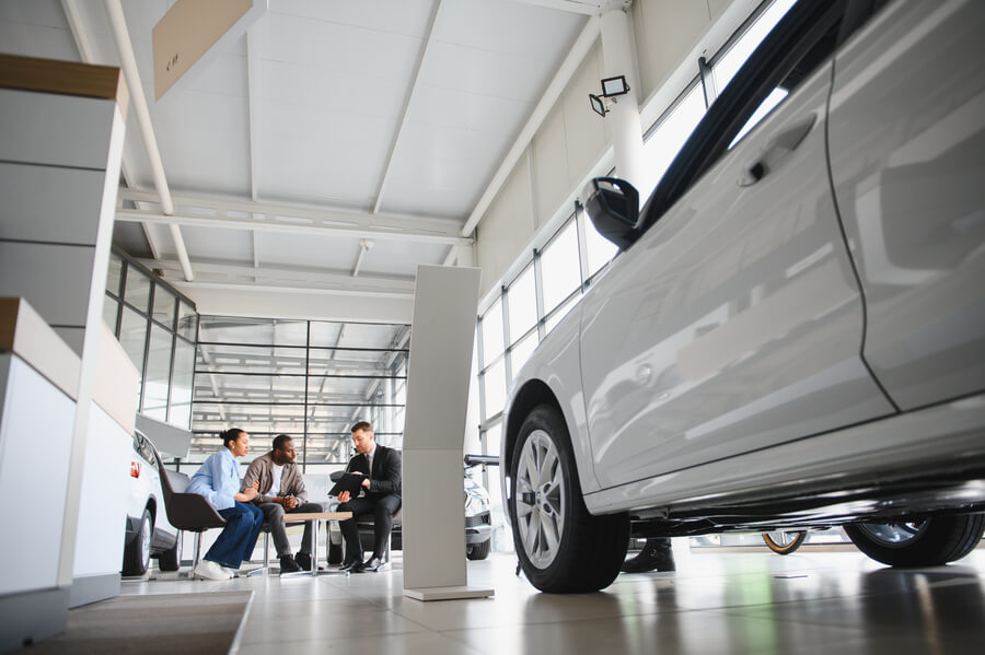 Low-angle view of cars inside a dealership showroom with customers talking.