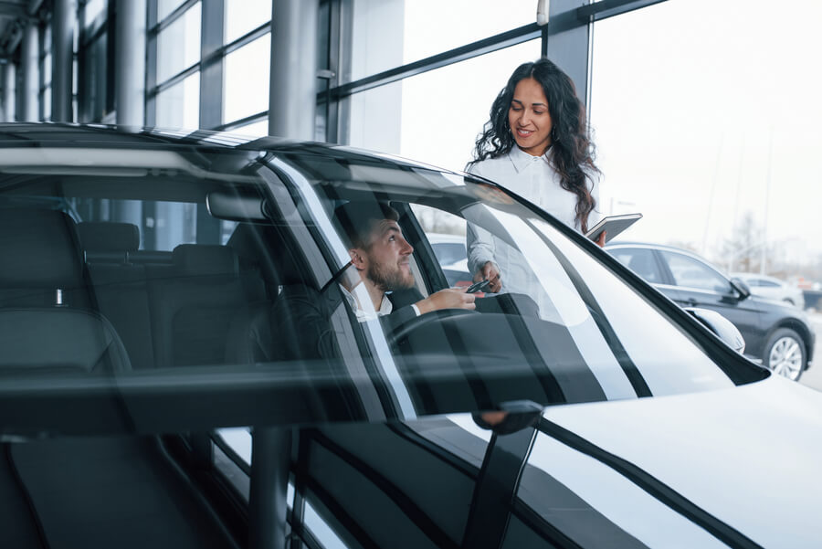 Sales consultant showing car features to a customer inside a dealership.