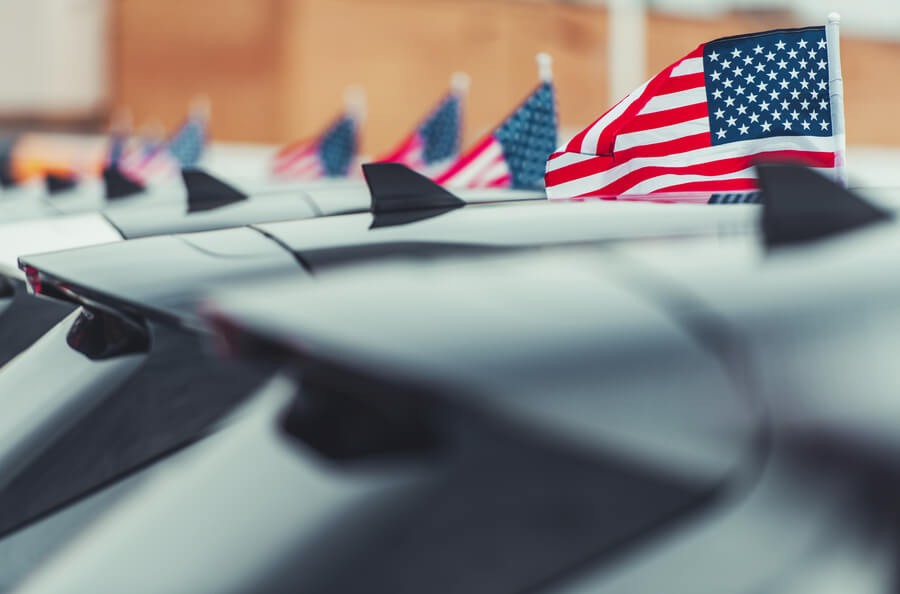 Small American flags displayed on cars at a dealership lot.