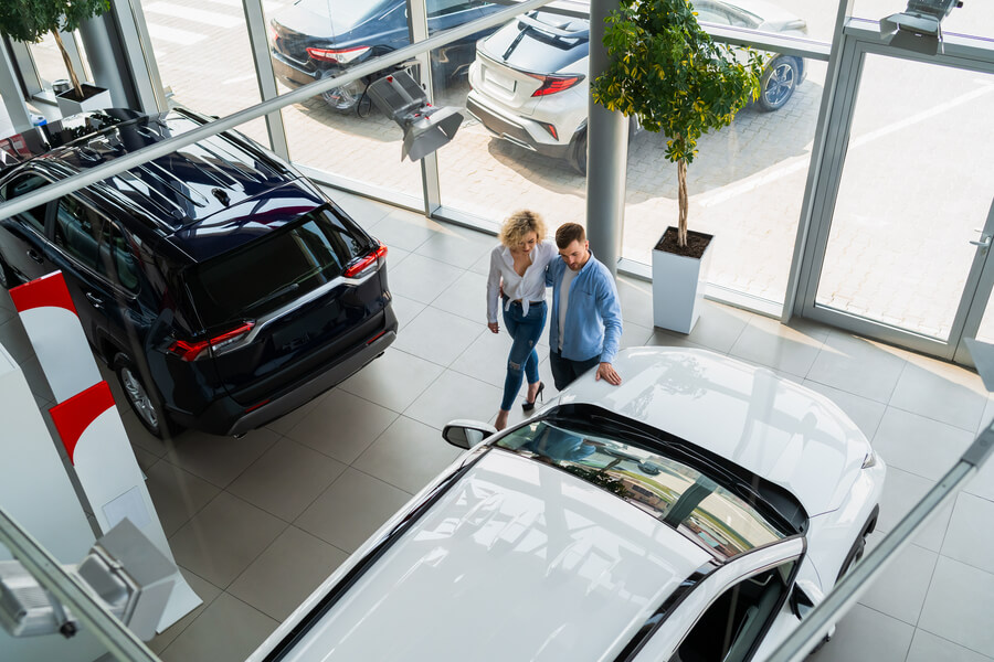 Couple walking through a car dealership showroom, viewing vehicles.