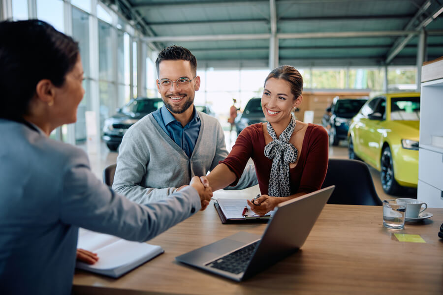 income tax refund advance - Couple shaking hands with a car salesperson.