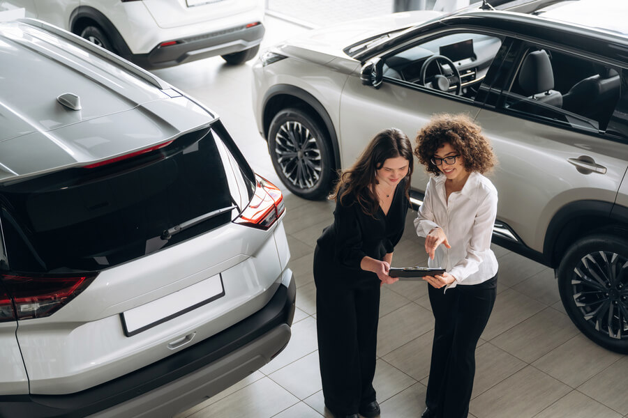 income tax refund advance - Two women reviewing details on a tablet in a car showroom.