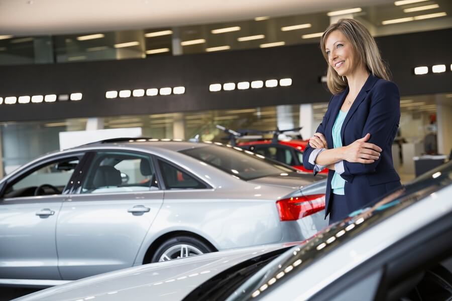 Woman holding car keys next to a new vehicle inside a dealership.