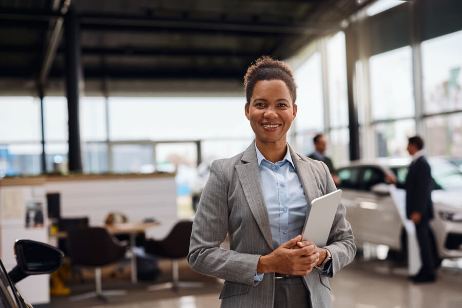 Smiling car sales consultant standing inside a dealership showroom.