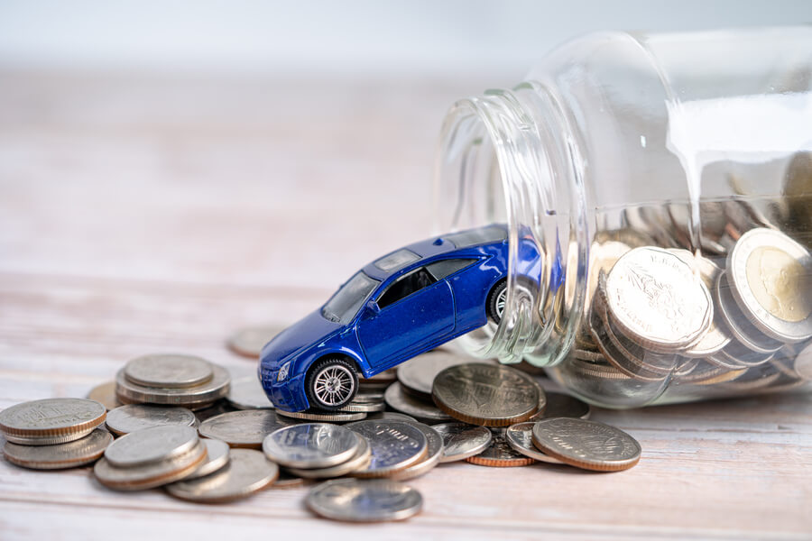 Income tax refund - Toy blue car on coins spilling from a glass jar.
