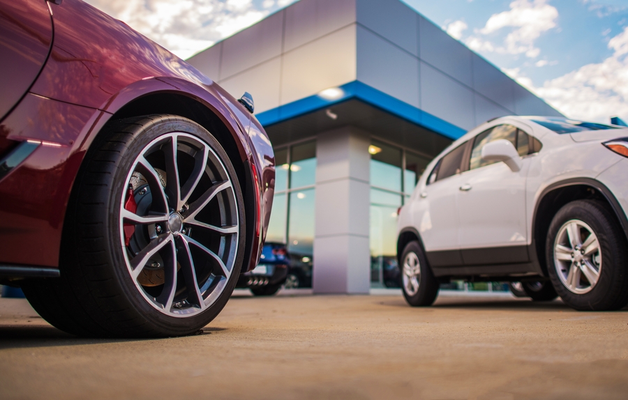 Is a tax refund income. - Two modern cars parked outside a contemporary building, with a close-up of a red car’s front wheel in the foreground and a white SUV near the entrance.