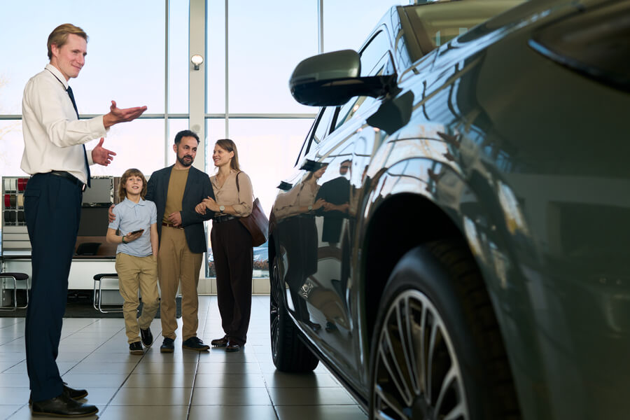 Sales consultant assisting customers near a car in a showroom.
