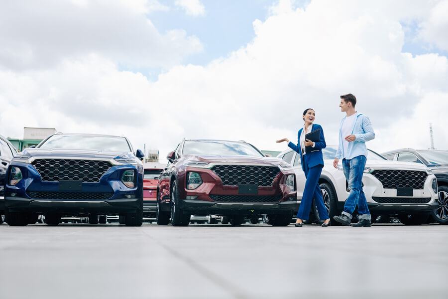 Couple standing in front of cars at a dealership lot.