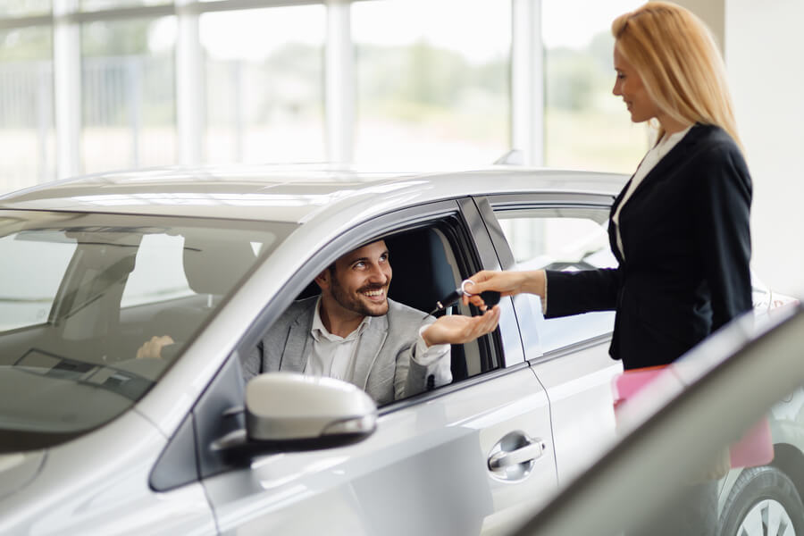 Sales consultant giving keys to a customer inside a car.