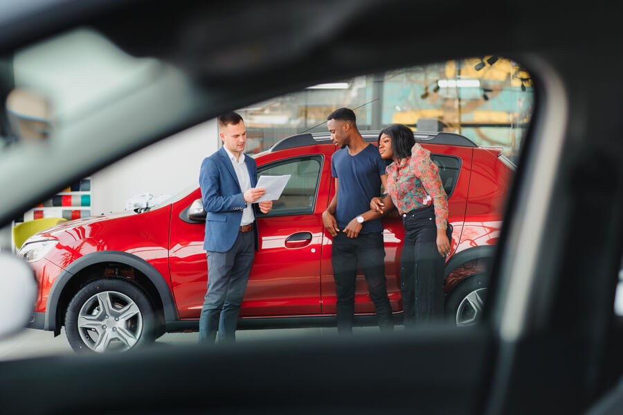 Customer inspecting a red car with a sales consultant at a dealership.
