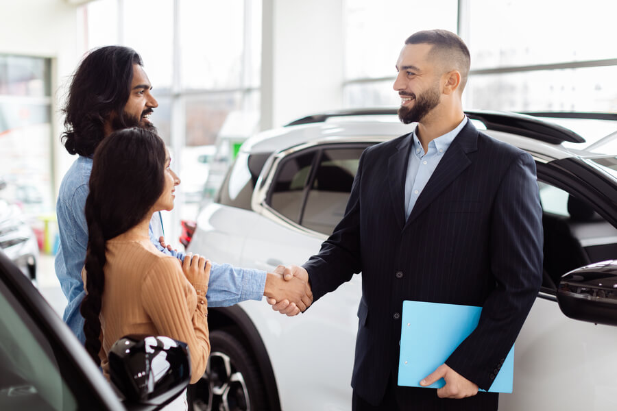 Sales consultant shaking hands with customers at a car dealership.
