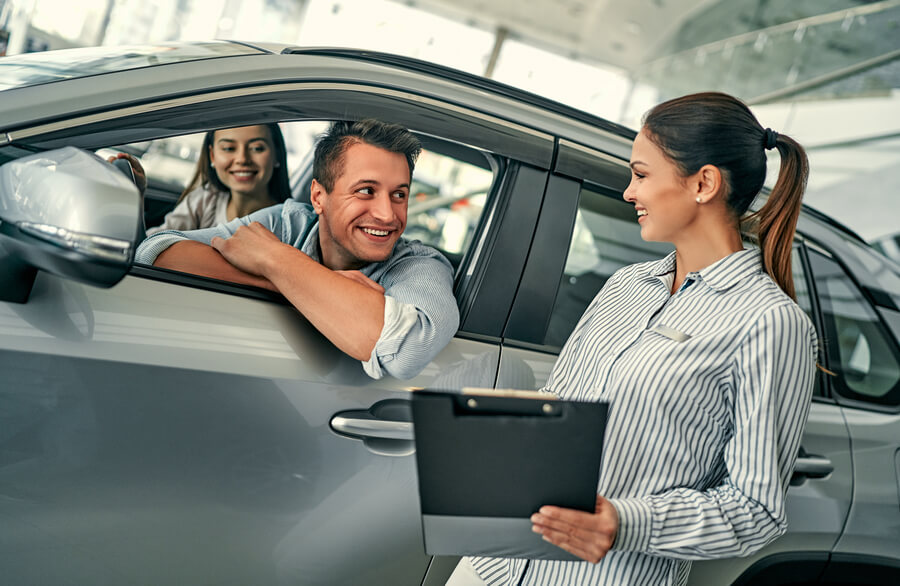 Sales consultant handing documents to a customer inside a car.