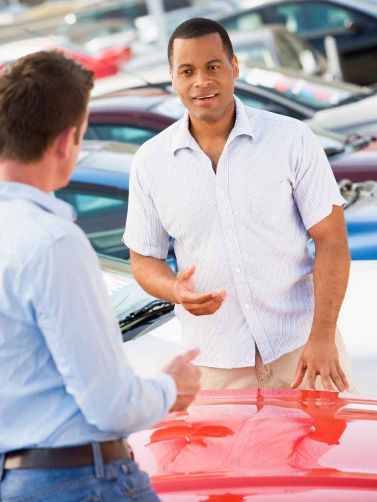 Man engaged in a conversation with a knowledgeable car salesman, discussing financing options at Auto Moto Deals dealership