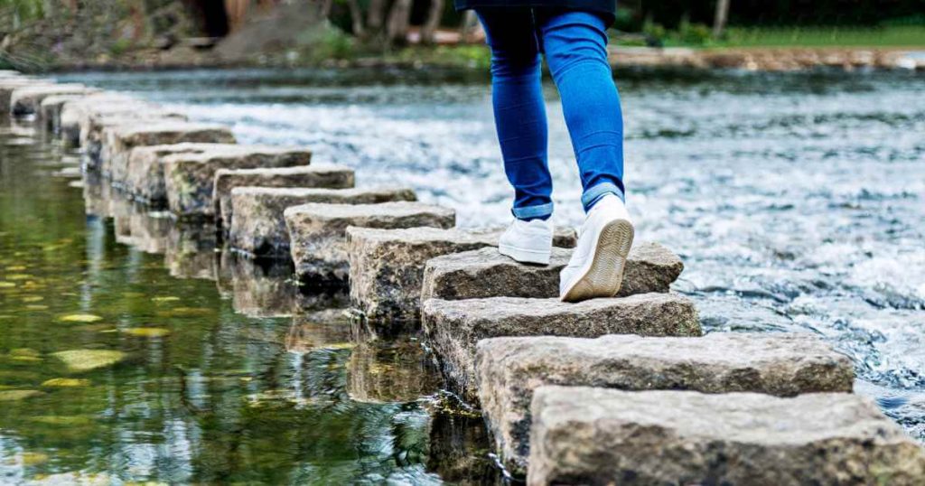 a woman walking on stepping stones depicting a buy here pay here dealership helping her