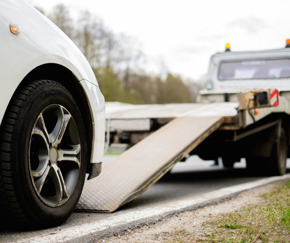 a tow truck with its ramp down ready to pick up a white car depicting a car repossession