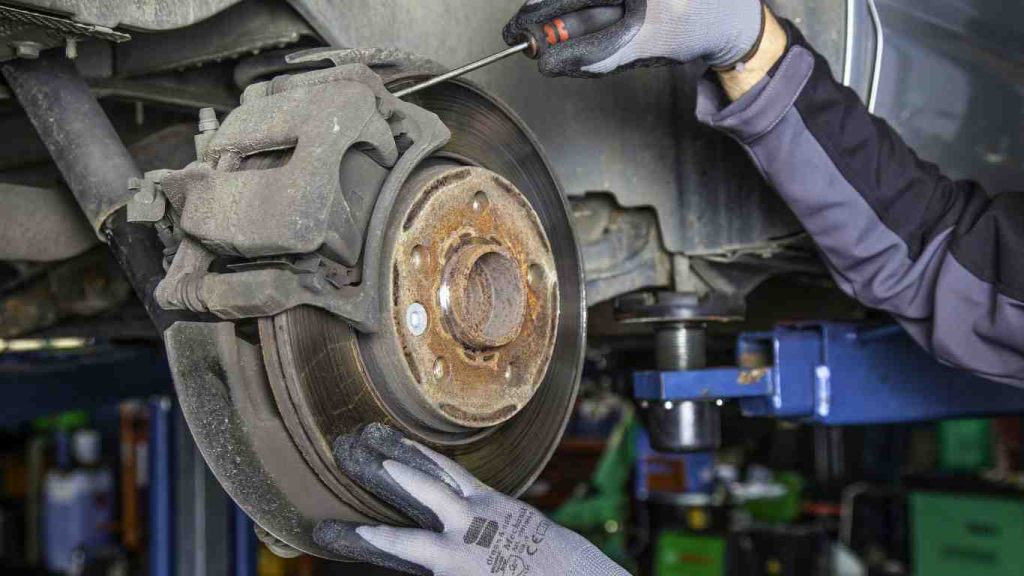 a service technician attempting to remove brake pads and rotors with severe rust and damage as he performs the brake maintenance for used cars