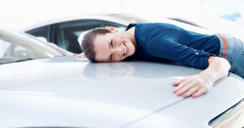 a woman hugging the hood of her car to show it some love