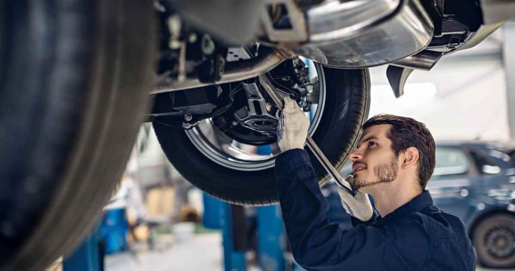 a man working on a used car with a car lifted in the air as he performs a car repair