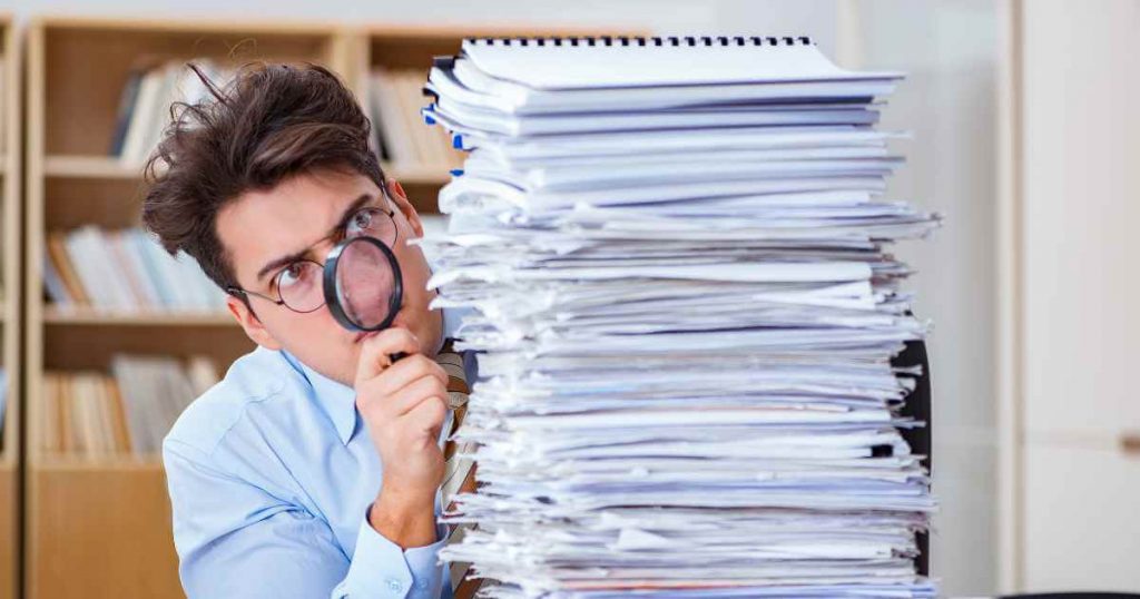 a man with a magnifying glass checking through a stack of papers