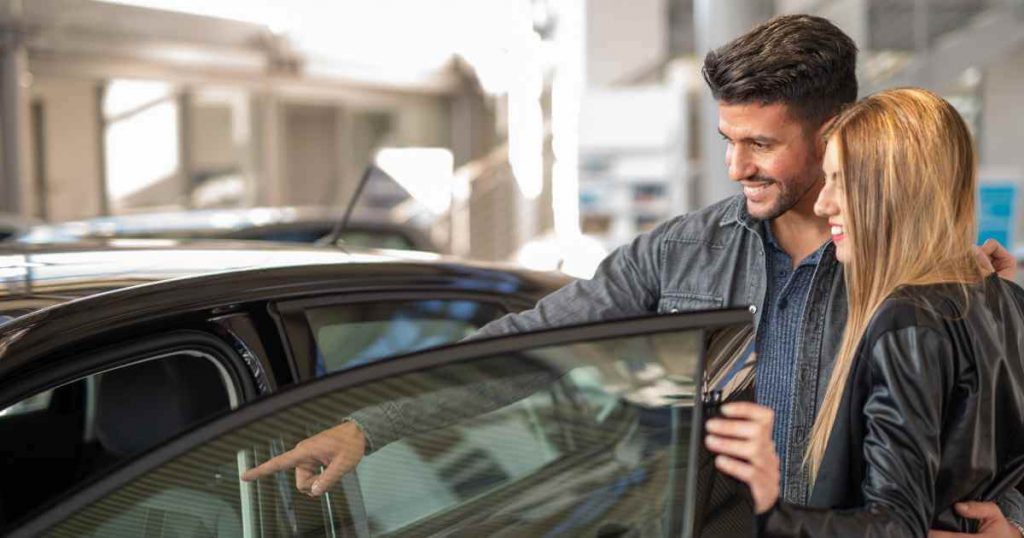 a man and a woman opening the car door and pointing inside as they choose a car dealership fresno offers them