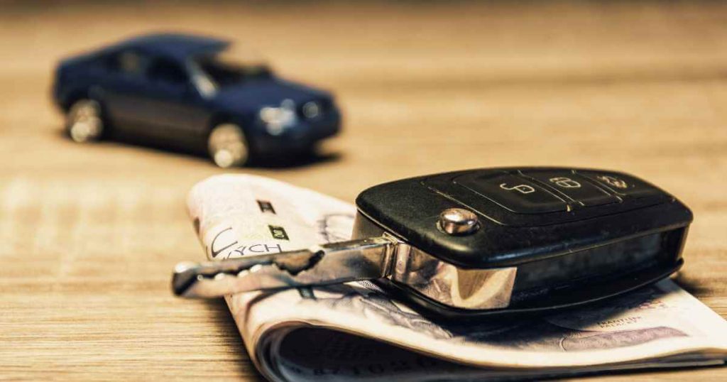 a car key on top of money with a toy car in the background