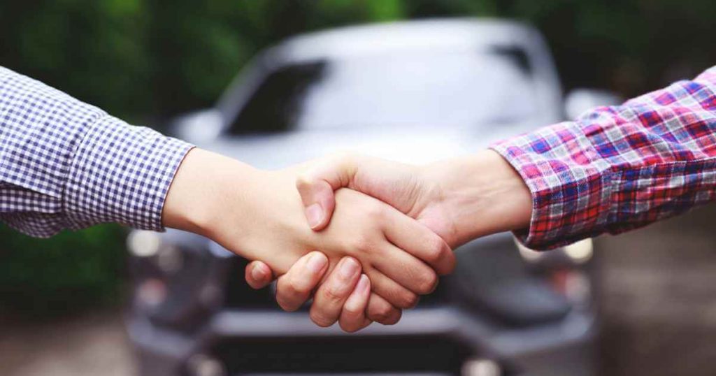 two people shaking hands after buying a car at a car lot no license needed