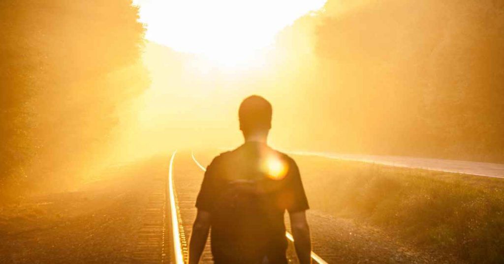 a man standing on a railroad track with the sun in front of him starting his journey toward a car dealership fresno has for him