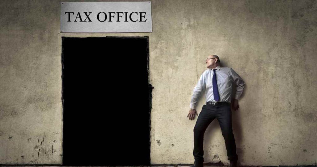 a man pressed up against a wall in fear of the tax office next to him