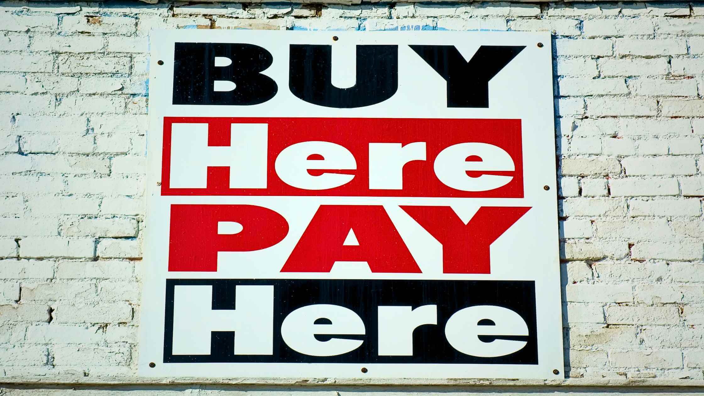 an image of a sign with the words "buy here pay here" on a brick wall
