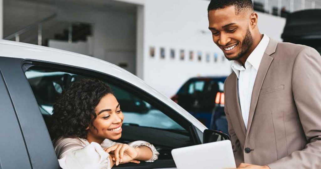 a picture of a man showing something on a paper to a woman leaning out of a car at a buy here pay here near me