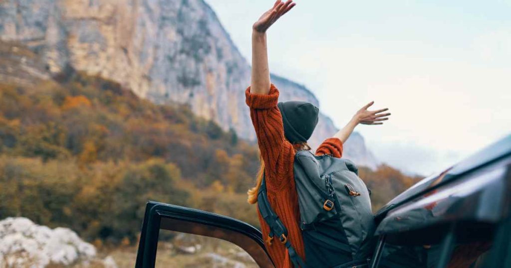 a picture of a woman with her arms up after arriving at the top of a mountain in a car she got from a buy here pay here near me