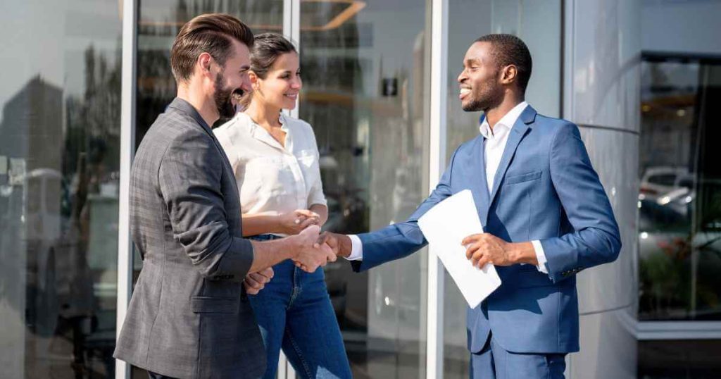 a photo of a couple shaking the hand of a car dealer
