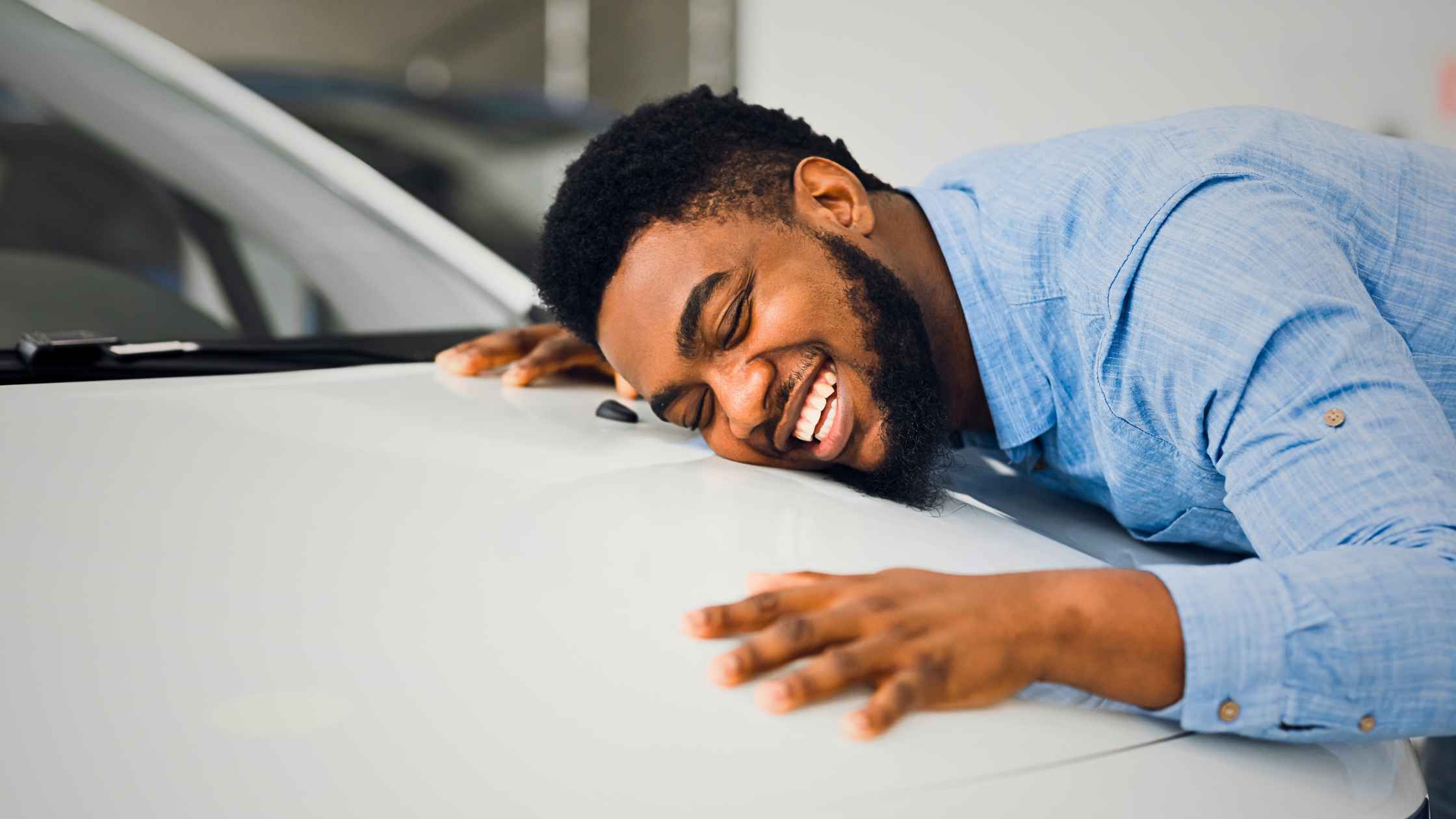 an image of a man with his eyes closed and a massive grin as he lays on the hood of a car that he got from one of the great dealerships near me