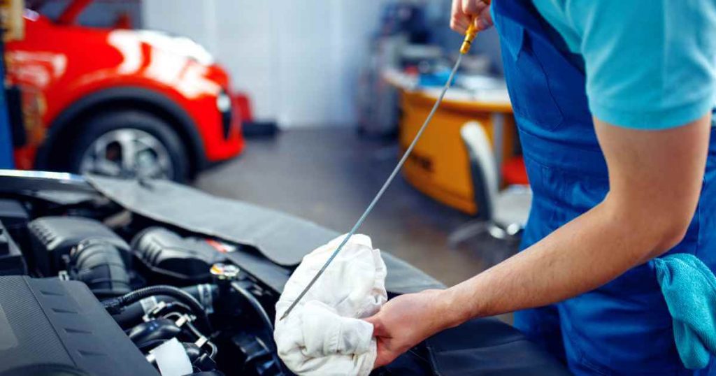 a person removing the oil dipstick from a used car to check the oil as part of regular car maintenance