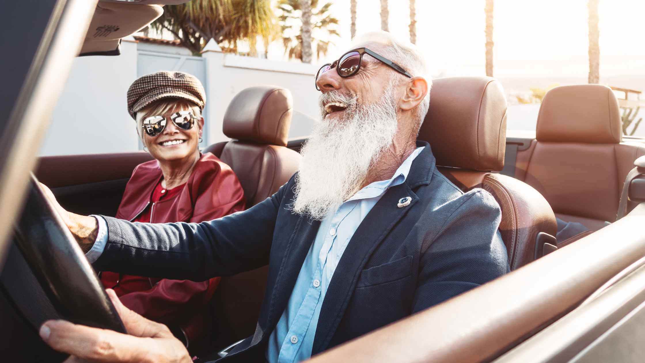 a photo of an older couple laughing in a new car with the convertible top down after going to a car dealership to do an old car trade in