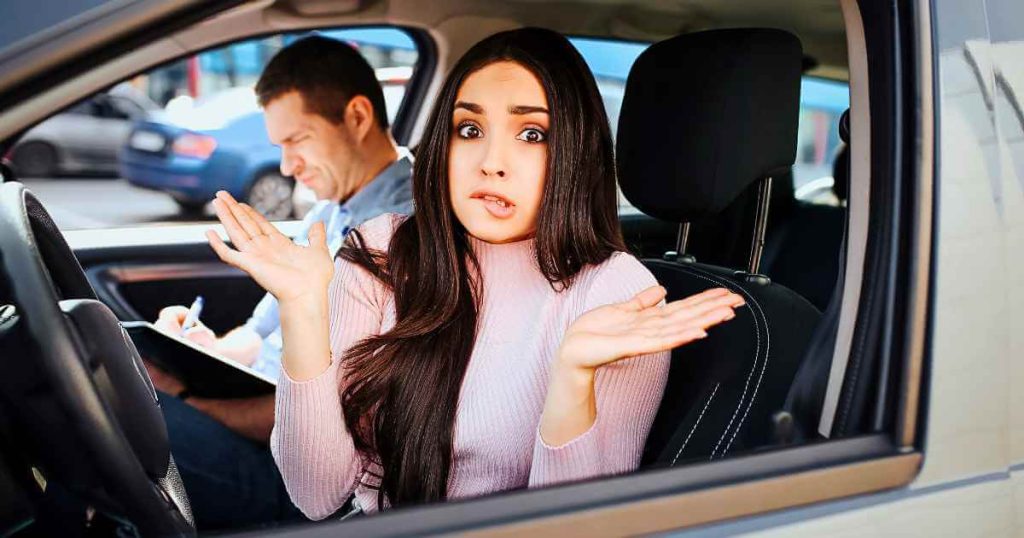 a photo of a girl in the driver's seat of a car with her hands up and biting her lip with a man behind her writing something down as she tries to do an old car trade