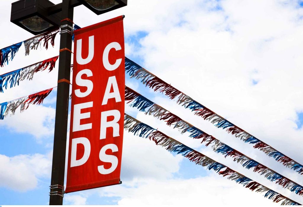 A photo of a used car dealerships lights, flags, and a sign saying "used cars"