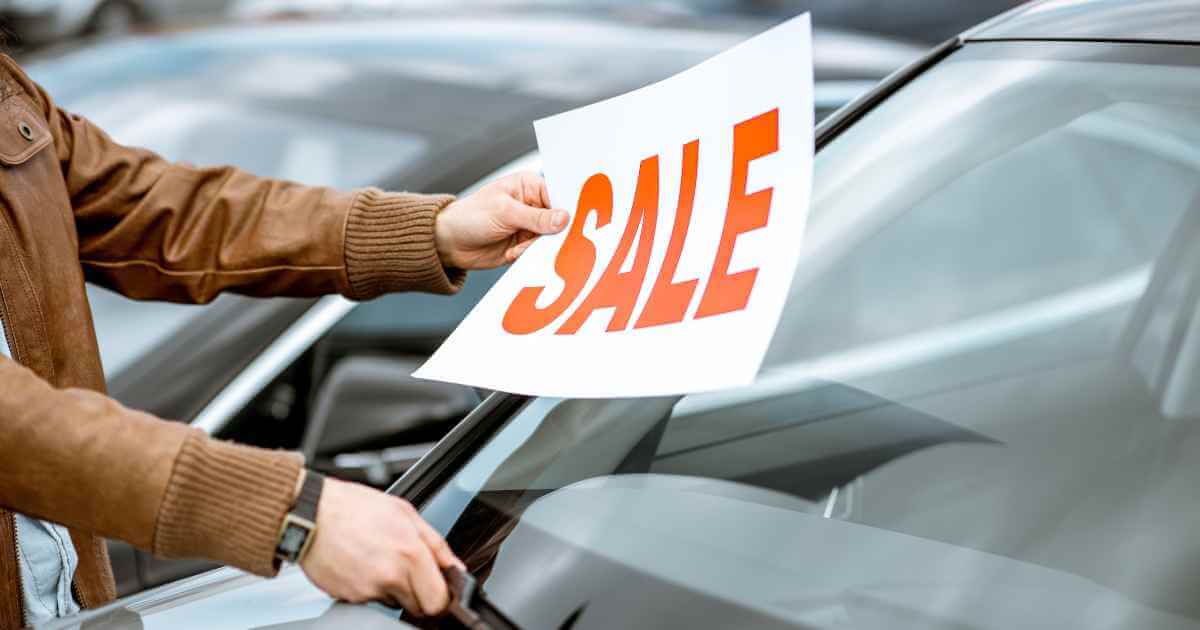 someone lifting windshield wipers to put a "sale" sign to show buying a used car on sale