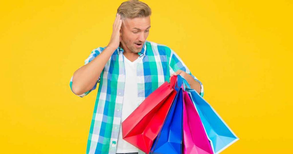 a man looking down at shopping bags in surprise as if he didn't prepare for his purchase