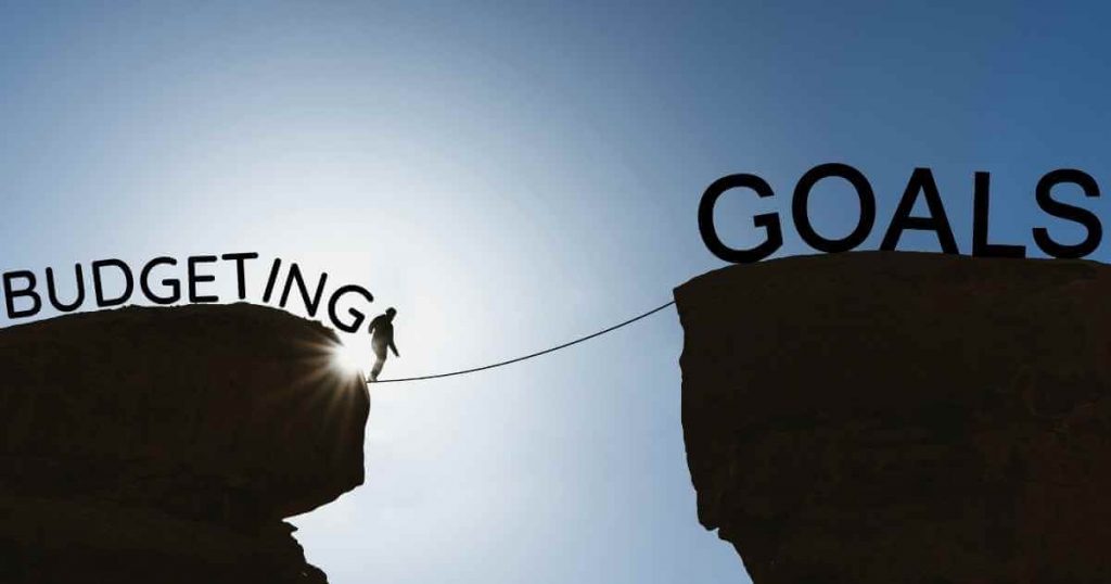 an image of a man walking a tightrope across two cliffs with the words budgeting behind him and goals in front